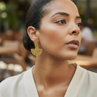 Woman wearing gold earrings with a blurred outdoor background
